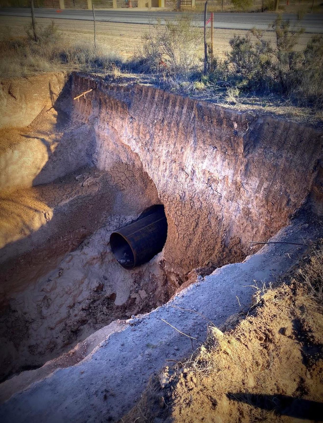 Steel casing pipe emerging from an excavation face beside a road